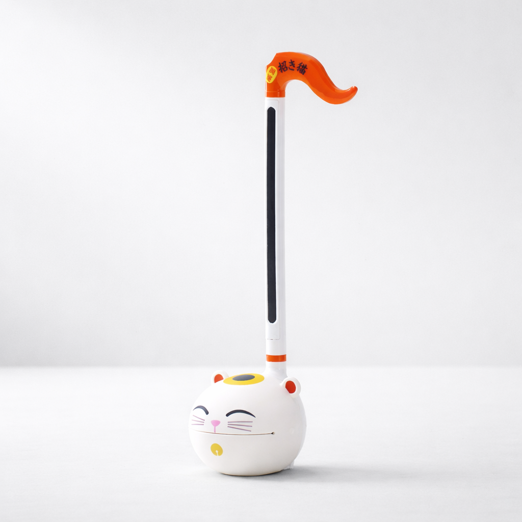 White Otamatone electronic musical instrument with a musical-note-shaped body and character face on a white background.
