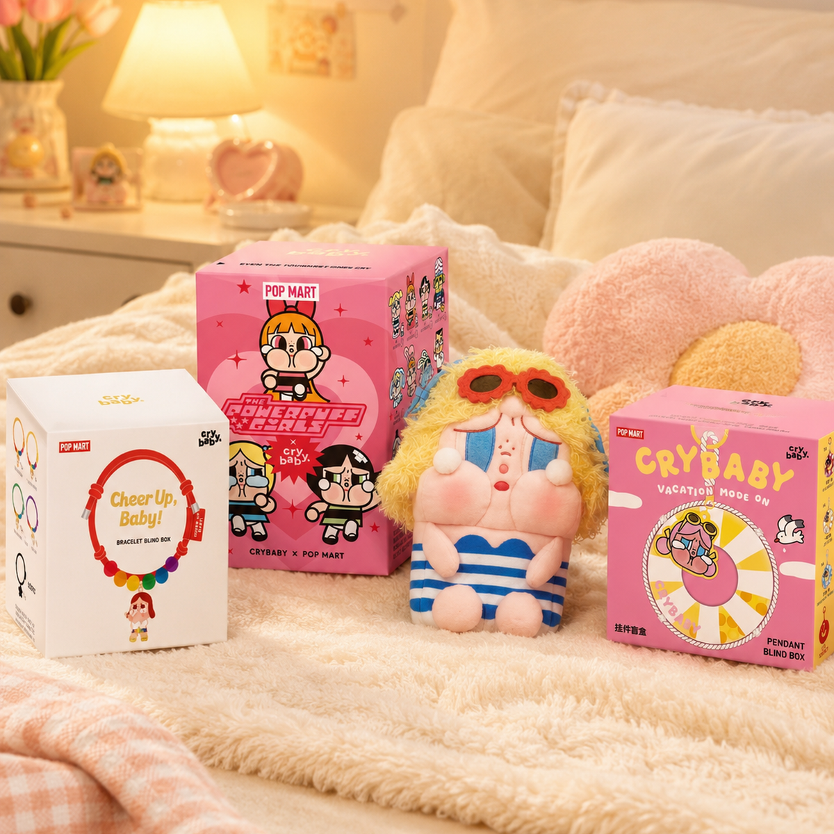 Three POP MART CRYBABY collectible plush toys displayed with colourful packaging on a beige blanket in a warm bedroom setting.